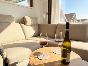 Ein gemütlicher Wohnbereich mit einer Couch, zwei Weingläsern und einer Weinflasche auf einem runden Holztisch.