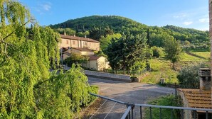 Ländliche Landschaft mit einem Steinhäuschen, einer gepflasterten Straße und einer Hügelkette im Hintergrund.