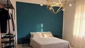 Ein Schlafzimmer mit Bett, einer Pendelleuchte, einer blauen Akzentwand und einem gemusterten Teppich.
