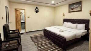 A bedroom with a bed, a chair, a clock, a ceiling fan, and a painting on the wall.