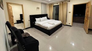 A bedroom with a bed, a desk, a chair, a TV, and a balcony.