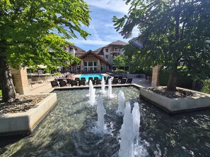 Un espace piscine agrémenté d’une fontaine, de chaises longues et d’un bâtiment à la façade en pierre.