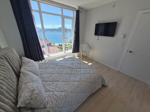 Une chambre avec un lit, une télévision, une chaise et une vue sur la mer.