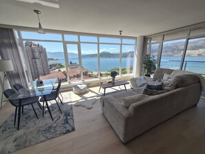 Un ampio soggiorno con una grande finestra che si affaccia su un lago e edifici.