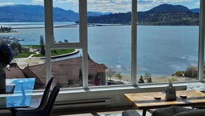 Ein Zimmer mit großem Fenster und Seeblick, einem Tisch mit Vase sowie einem Sessel.
