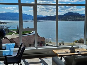 Ein Zimmer mit großem Fenster und Seeblick, einem Tisch mit Vase sowie einem Sessel.