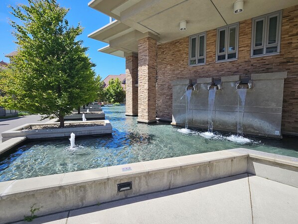 A water feature with a fountain and a tree in front of a building with stone and brick facade. - STUNNING LAKEVIEW LUXURY (Kelowna)