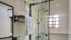 A modern bathroom with a glass shower enclosure, a white toilet, a sink, and a towel rack. - JOYZY HAVEN LUXURY SERVICE APARTMENT  (Ibadan)