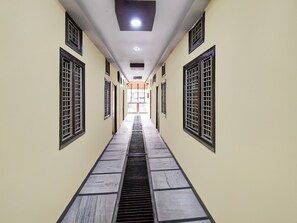 A corridor with tiled flooring, a central drain, and windows with metal grilles on both sides.