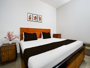A hotel room with a wooden headboard, a large bed with white and black bedding, a nightstand with a vase of flowers, and three framed pictures on the wall.