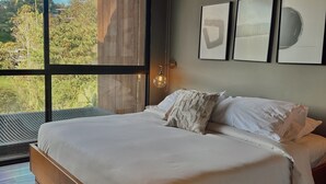 Une chambre avec un grand lit, une vue sur la verdure et trois œuvres d’art encadrées accrochées au mur.