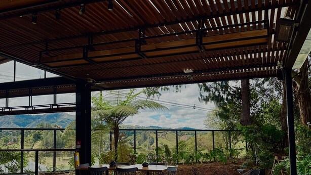 Une terrasse extérieure avec des tables et des chaises en bois, un canapé gris et une vue sur un paysage montagneux.