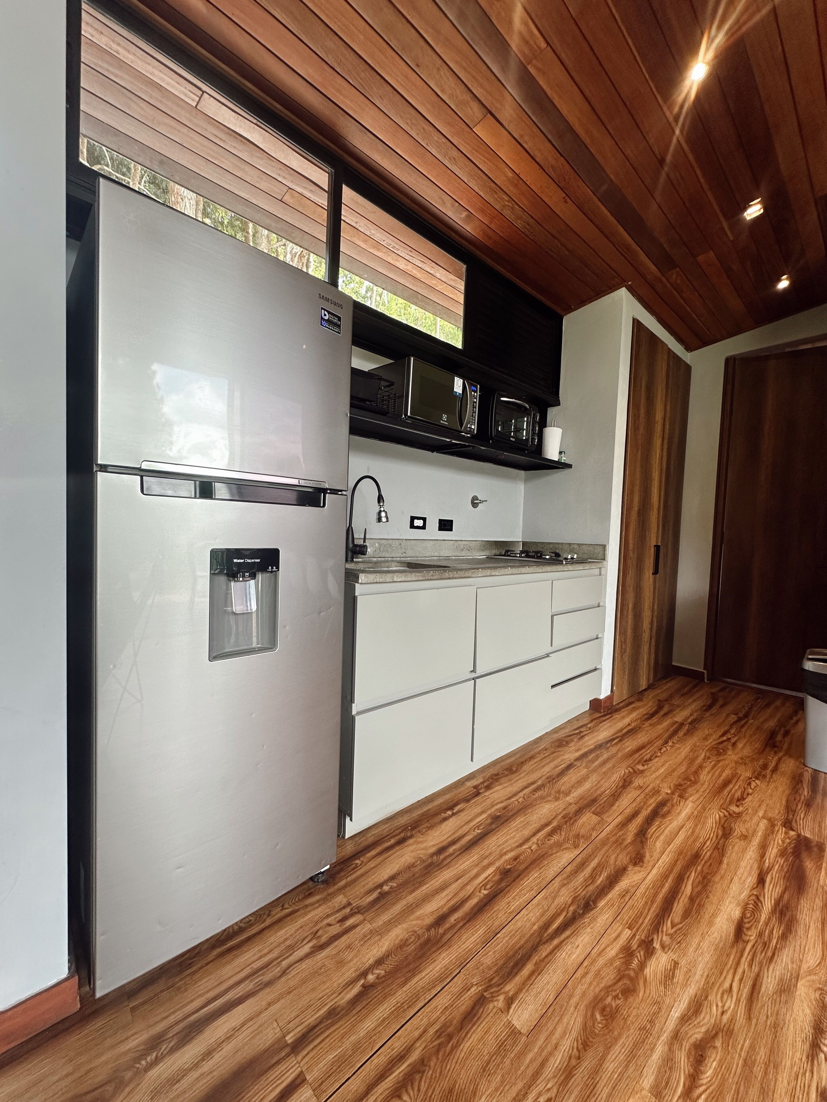 A modern kitchen with a stainless steel refrigerator, microwave, and oven, wooden flooring, and a wooden ceiling.