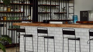 Un espace bar avec un comptoir en bois, des chaises en métal noir et des luminaires sphériques suspendus.