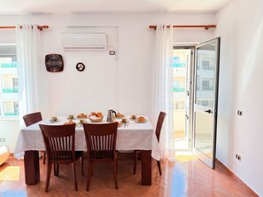 A dining area with a table set for breakfast, chairs, an air conditioning unit, and a view through a glass door. - Cozy Apartment 70 meters from Durres Beach (Durres)