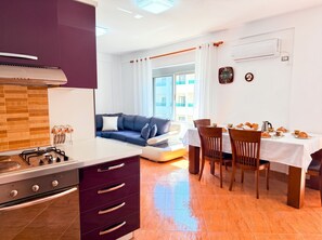 A modern kitchen with a gas stove, a dining area with a table set for breakfast, a sofa, and a large window with curtains. - Cozy Apartment 70 meters from Durres Beach (Durres)
