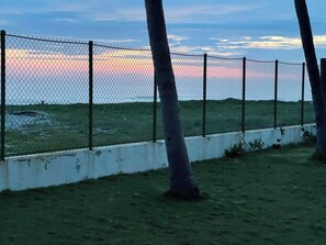 Ein Maschendrahtzaun mit Bäumen im Vordergrund und einem Sonnenuntergang im Hintergrund.