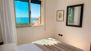 A bedroom with a bed, a window with a view of the sea, a framed picture, and a mirror. - Holiday Home by the Beach Durres 117 (Durres)