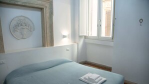 Une chambre à coucher avec un lit, une fenêtre, une lampe fixée au mur et une assiette décorative.