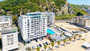 A multi-story hotel with a rooftop pool, surrounded by parking and palm trees. - Beachfront- Sea View Holiday Home 105 (Durres)