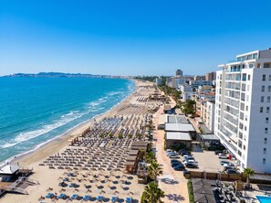 Un hôtel situé en bord de mer, avec des rangées de chaises longues, une piscine et une vue sur l’océan.