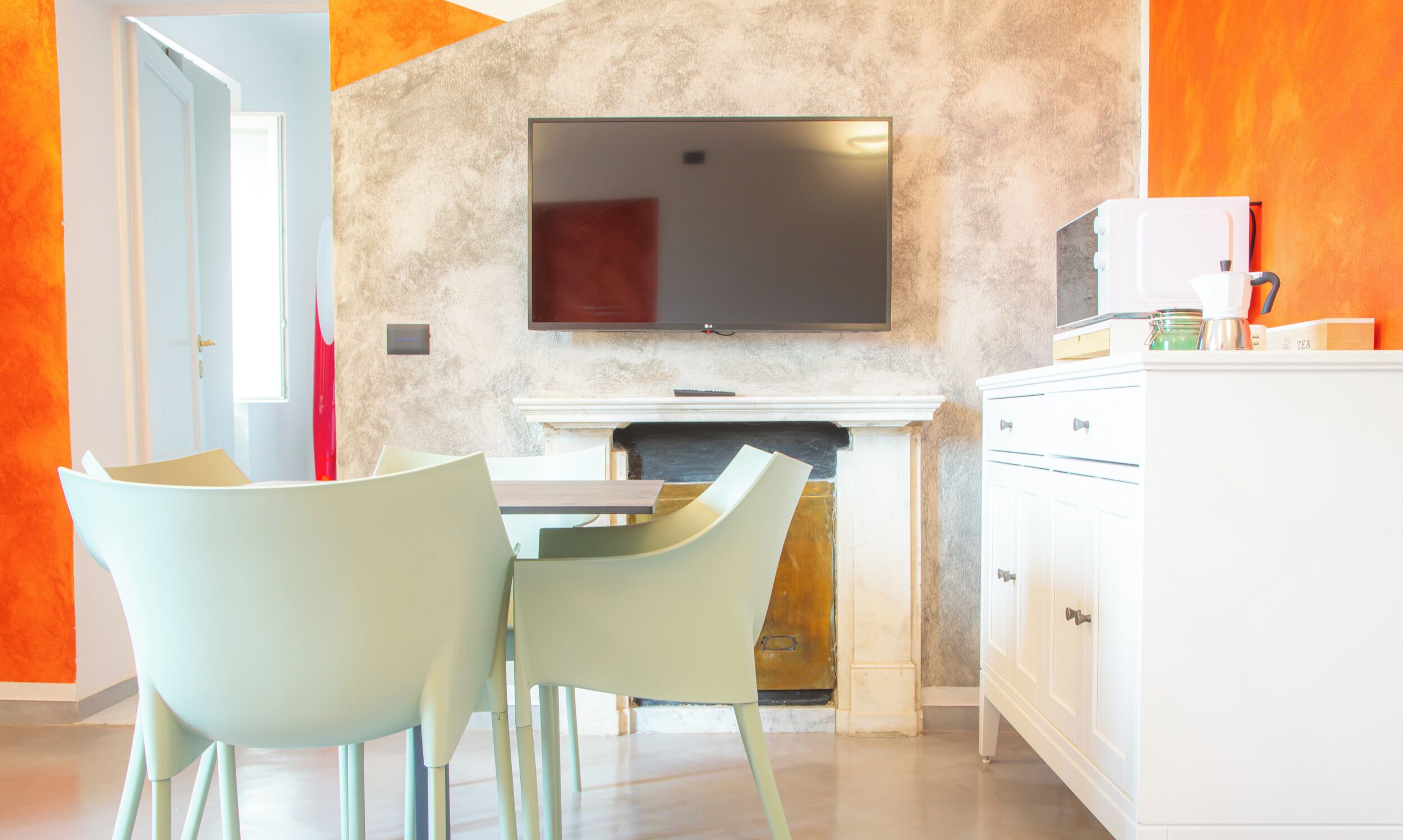 Una cocina moderna con un televisor de pantalla plana sobre una chimenea, sillas de color claro y armarios blancos.
