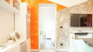 A modern kitchen with a TV, white cabinets, and a bright orange accent wall. - Quiet and Central: Discover Pisa on Foot (Pisa)