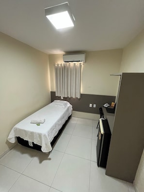 A small, clean room with a single bed, a desk, an air conditioner, and a curtain. - GRACE PALACE HOTEL (Sobral)
