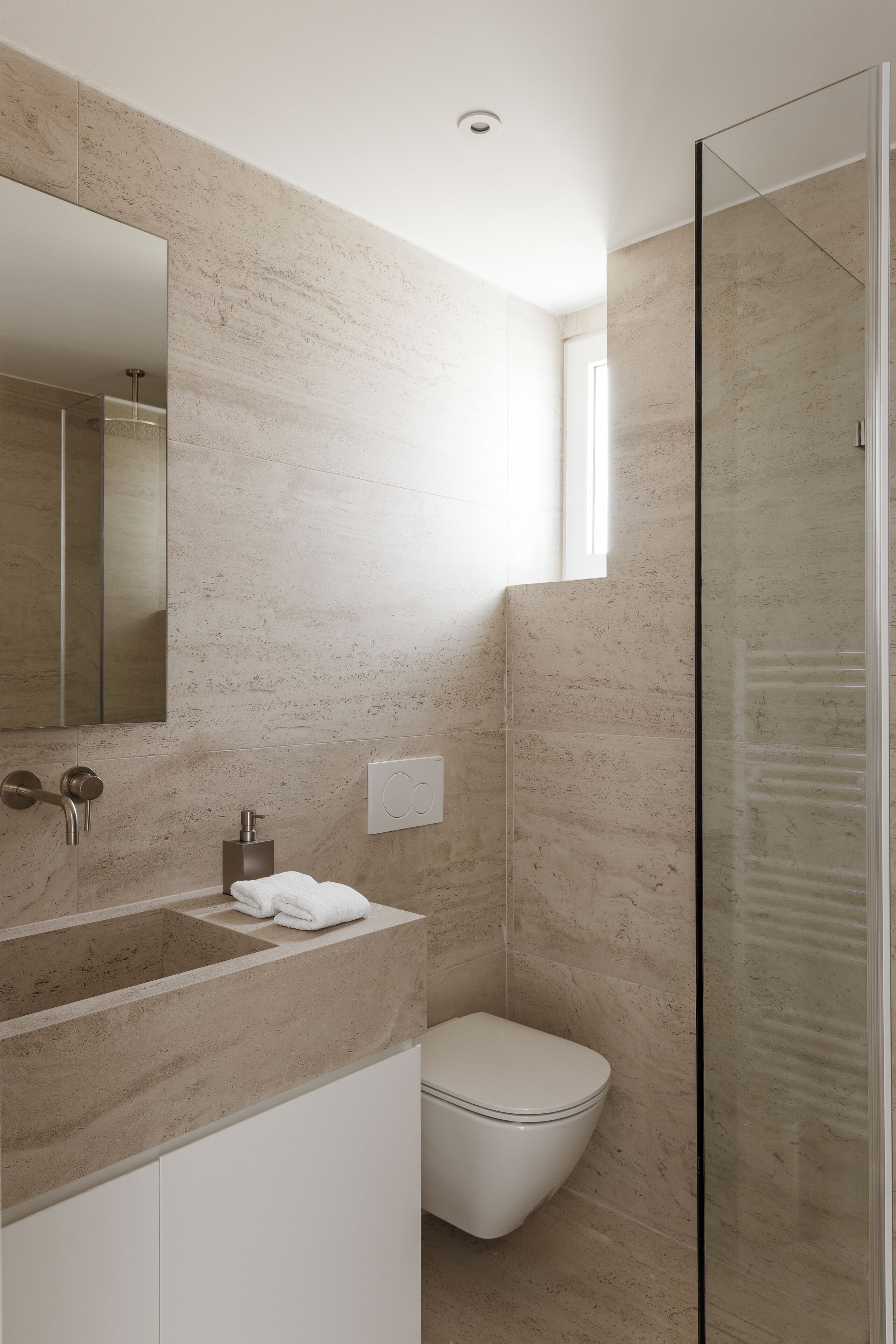A modern bathroom with a marble sink, a toilet, and a glass shower enclosure.