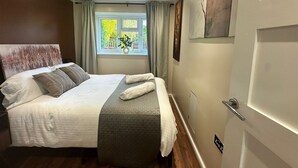 Un dormitorio con cama, una ventana con cortinas, una puerta y un cuadro colgado en la pared.