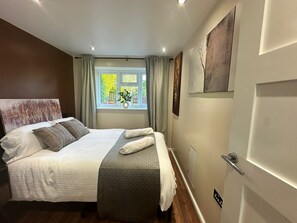A bedroom with a bed, a window with curtains, a door, and a wall-mounted artwork. - Modern Bromley Stay with Parking, Wi-Fi & Garden (Greater London)