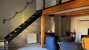 Ein Lofts-Wohnraum mit Holzboden, einer Holztreppe, einem Sofa, einem Esstisch und einer Heizung.