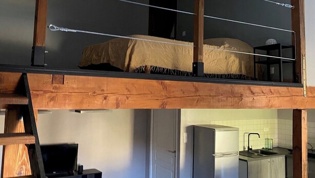 Ein Loft-Zimmer mit Stockbett, Schreibtisch, Stuhl und einer Küchenzeile.