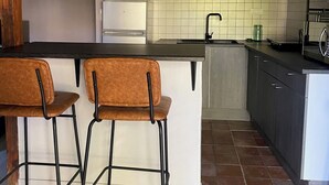 Eine Küche mit Barbereich, zwei Barhocker, einem weißen Kühlschrank, einer gefliesten Spritzschutzwand und Holzbalken.