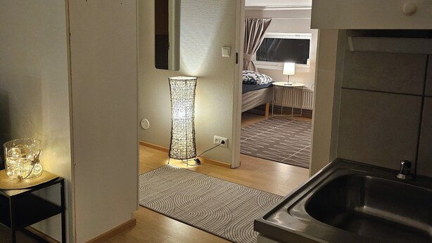 Eine moderne Küche mit Spüle, ein Essbereich mit Tisch und Stühlen sowie ein Flur, der zu einem Schlafzimmer mit Fenster führt.