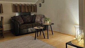 Ein Wohnzimmer mit einer Couch, einem kleinen runden Tisch, einer Stehlampe und einem gemusterten Teppich.