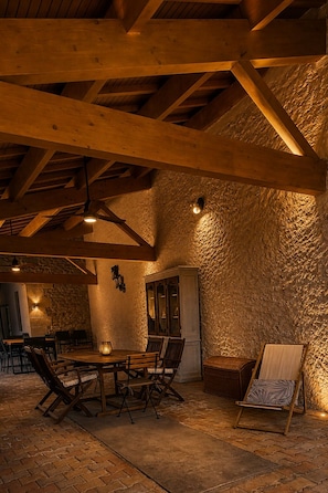 A rustic interior with exposed wooden beams, a stone wall, and a dining area with a table and chairs.