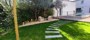 Un giardino curato con un vialetto in pietra, due zone relax all'aperto e una piscina.