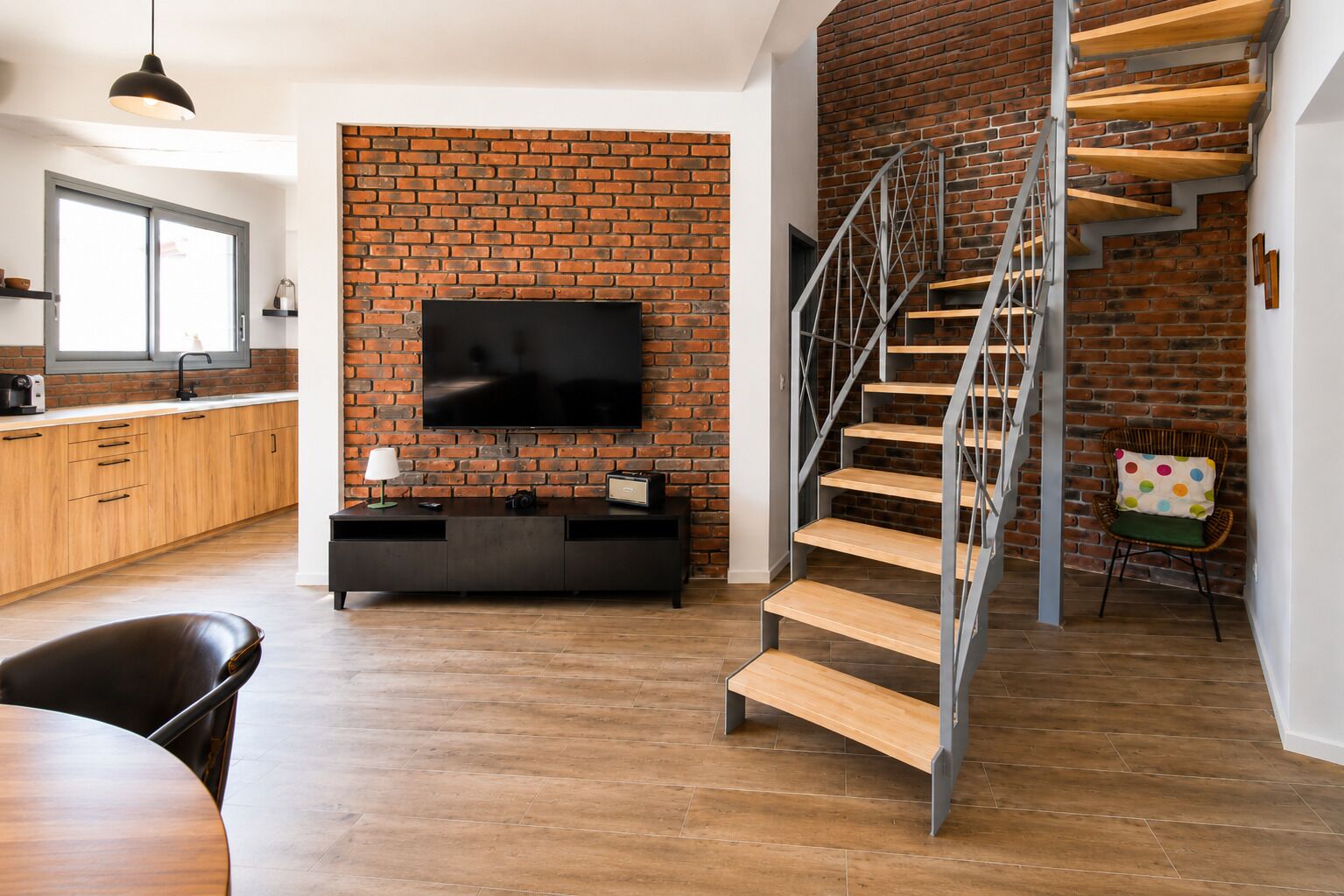 Un espace de vie moderne avec un mur en briques, un téléviseur à écran plat, un escalier en bois et un coin repas.