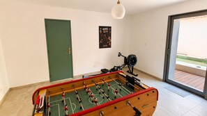 Ein Zimmer mit Kicker, einer Tür, einem Poster an der Wand und einem Fenster mit Blick.