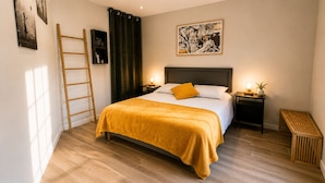 Ein Schlafzimmer mit Bett, Nachttisch, einer Leiter, einem Bildrahmen und einem Vorhang.