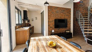 Eine moderne Küche mit Backsteinwand, eine Essecke mit Holztisch und eine Treppe mit Metallgeländer.