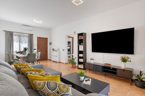 Ein modernes Wohnzimmer mit Sofa, Couchtisch, Flachbildfernseher und einem Essbereich mit Stühlen und Tisch.