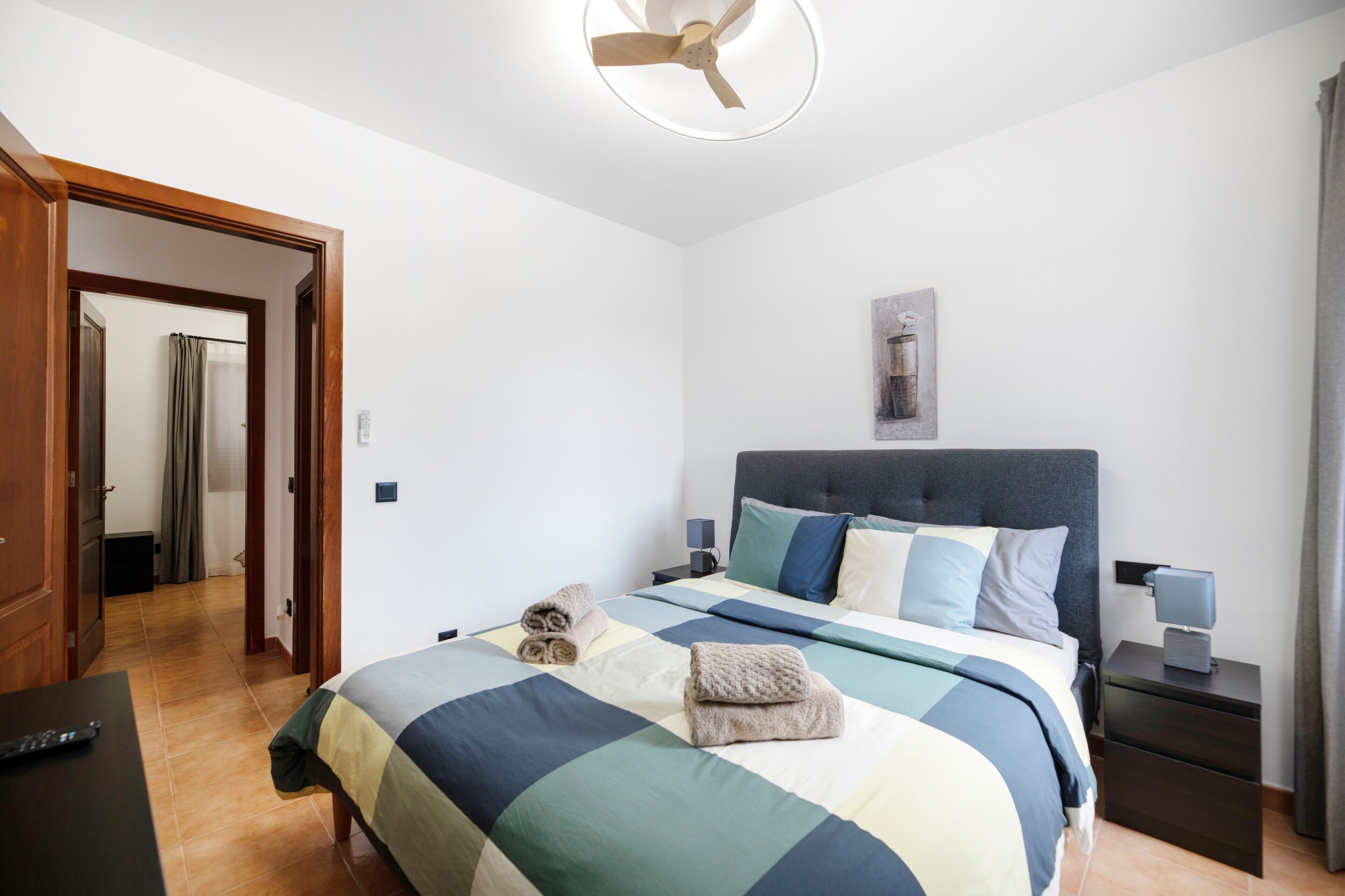 A bedroom with a bed, bedside tables, a ceiling fan, and a door leading to a bathroom.