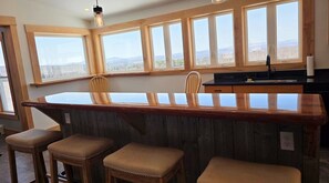 A bar area with wooden stools, a counter, and large windows with a view. - Sunsets Await! Fully renovated farmhouse with green mountain views (Barton)