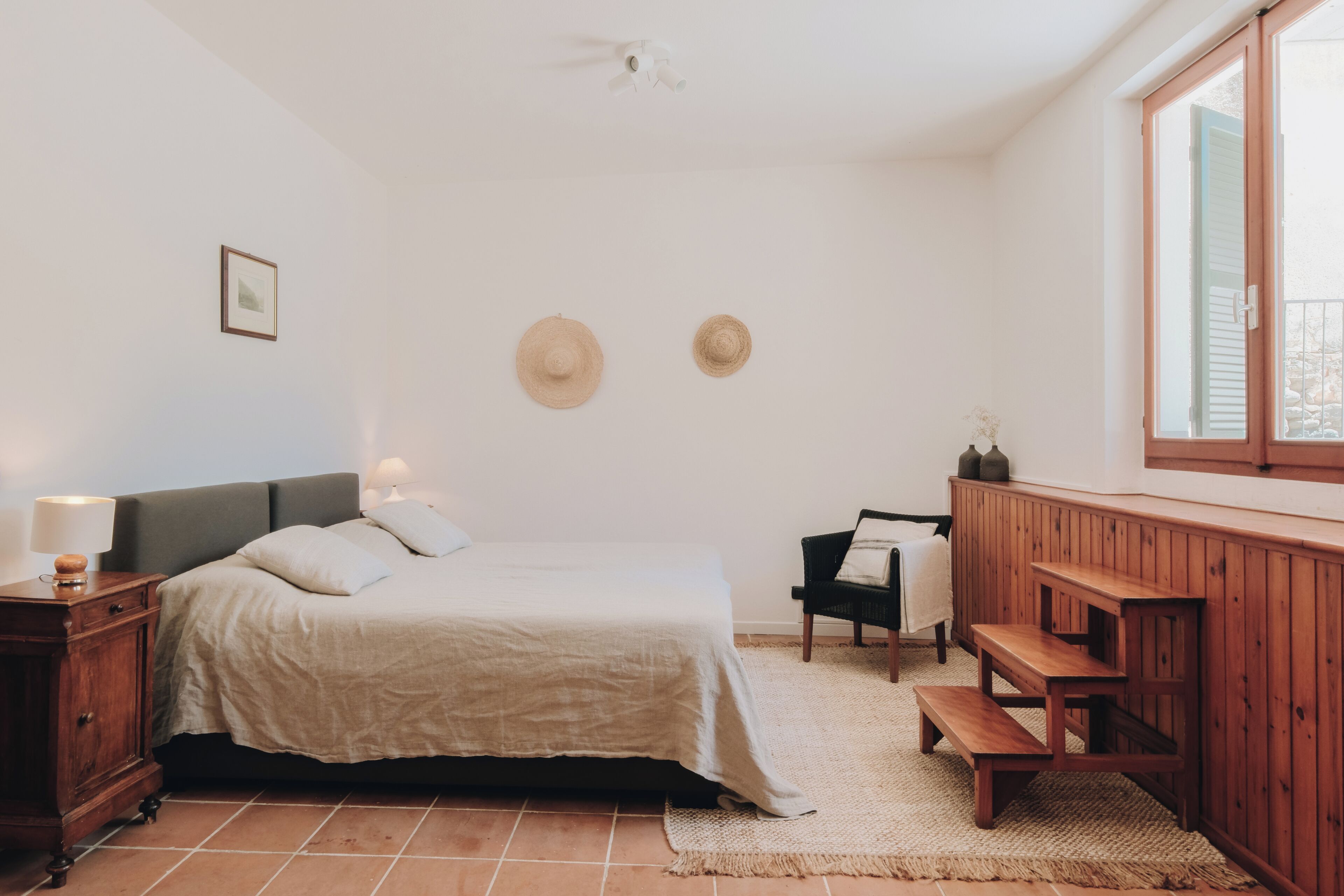 A bedroom with a bed, bedside tables, a bench, a window, and a wall-mounted picture.