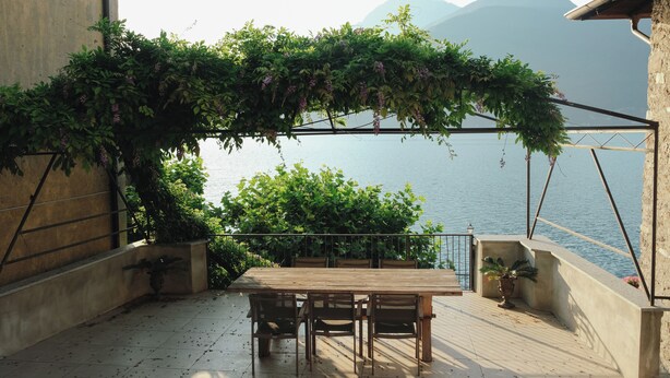 A terrace with a wooden table and chairs, a pergola with greenery, and a view of a body of water and mountains. - Authentic house with beautiful view of lake como (Musso)