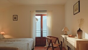 A room with a bed, a chair, a desk, a lamp, a vase, and a door leading to a balcony. - Authentic house with beautiful view of lake como (Musso)