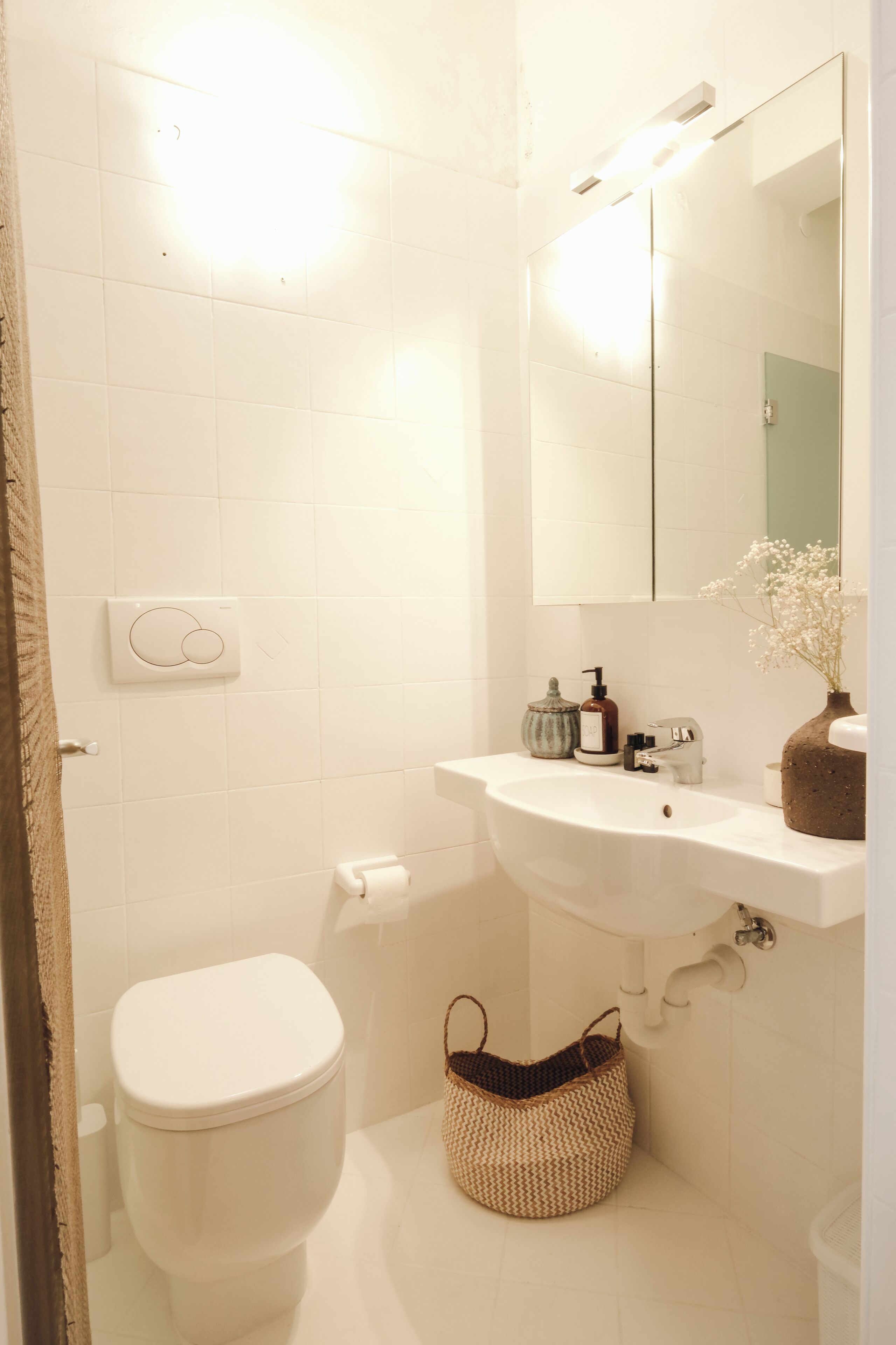 Et badeværelse med toilet, vask, spejl og vægmonteret lysarmatur.