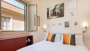 Hotellihuone, jossa on sänky, ikkuna, punainen kaappi ja seinätaideteoksia.